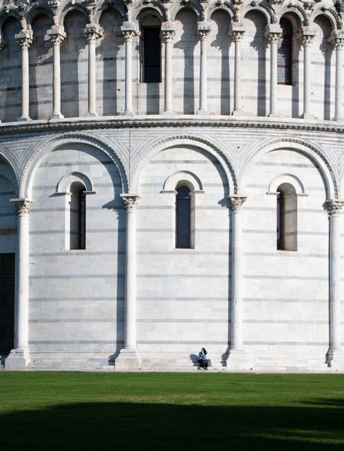 Free The Pisa Baptistery in Tuscany, Italy, featuring its ornate facade with a person seated for scale. Stock Photo