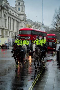 Mounted police patrolling a rainy street in London with red buses and historic architecture.