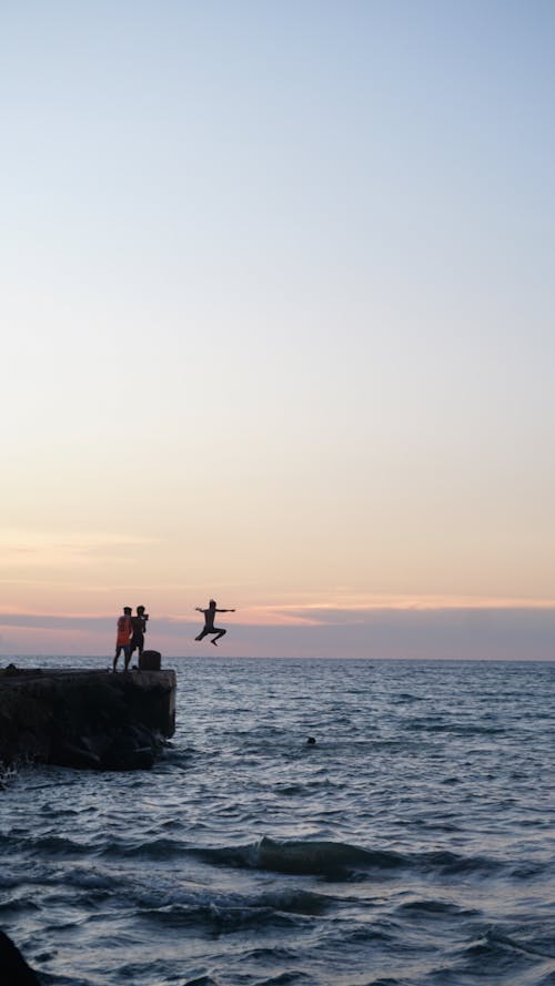 Silhouettes of People Jumping into the Sea at Sunset