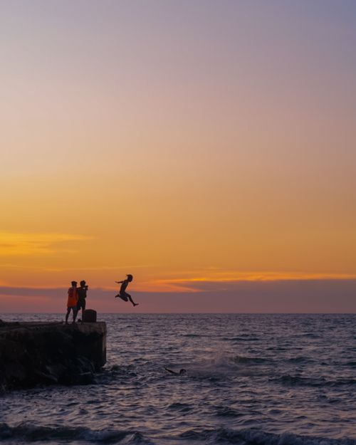 Free A person jumps off a pier into the sea during a vibrant sunset, capturing adventure and freedom. Stock Photo