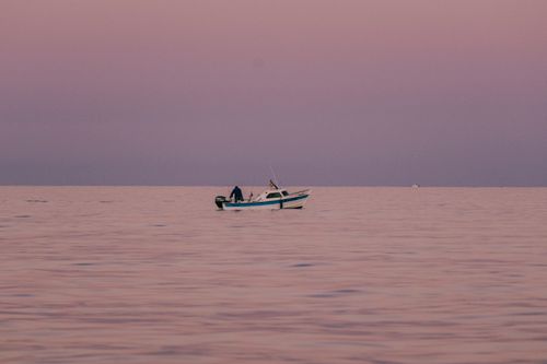 Free A solitary fishing boat in the calm pink hues of the ocean at dusk, capturing tranquility. Stock Photo