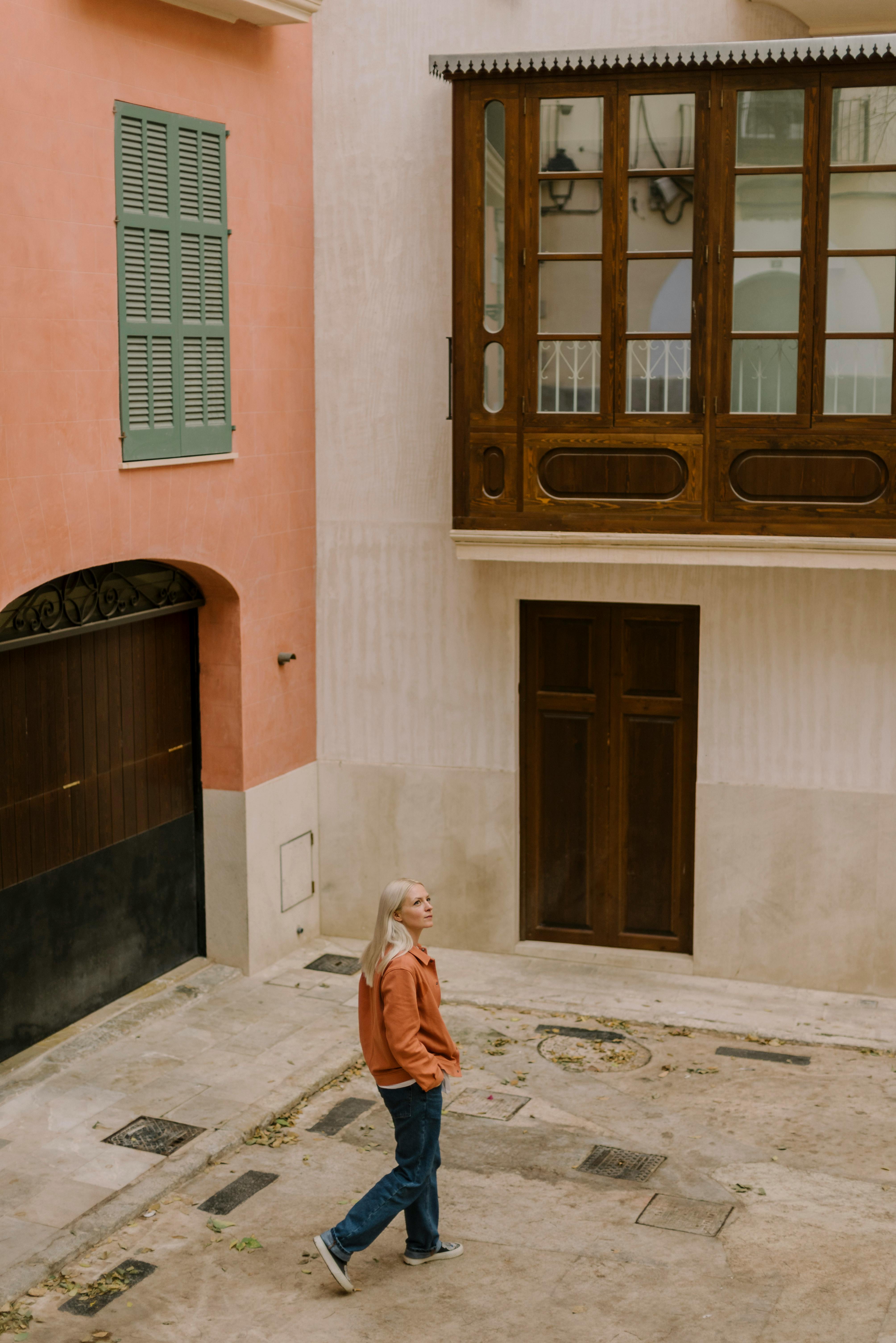 A young woman walking in a quaint European courtyard, exuding charm and architectural appeal.