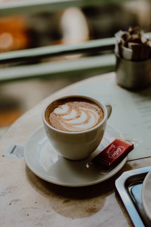 Free Cozy café setting featuring a cappuccino with latte art on a marble table. Stock Photo