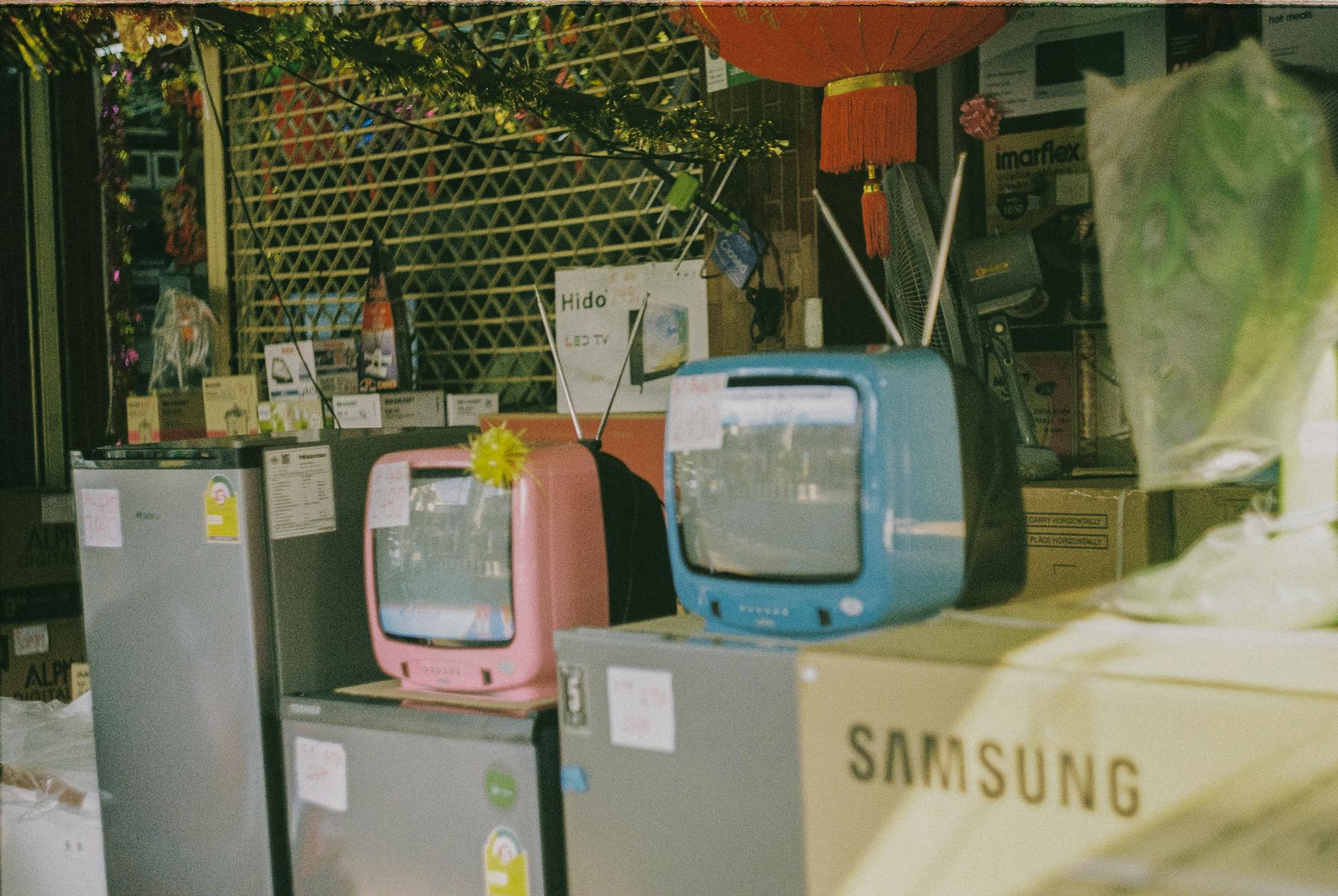 A storefront display featuring vintage televisions and home appliances on a sunny day in Bangkok.