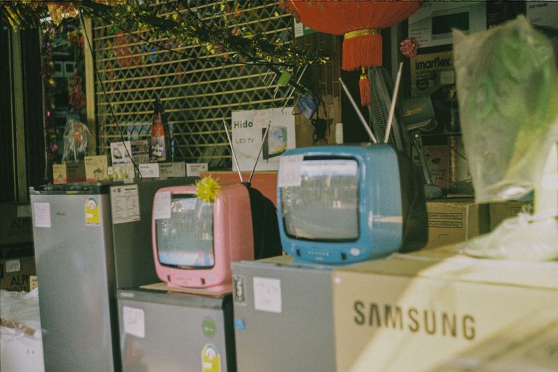 A storefront display featuring vintage televisions and home appliances on a sunny day in Bangkok.