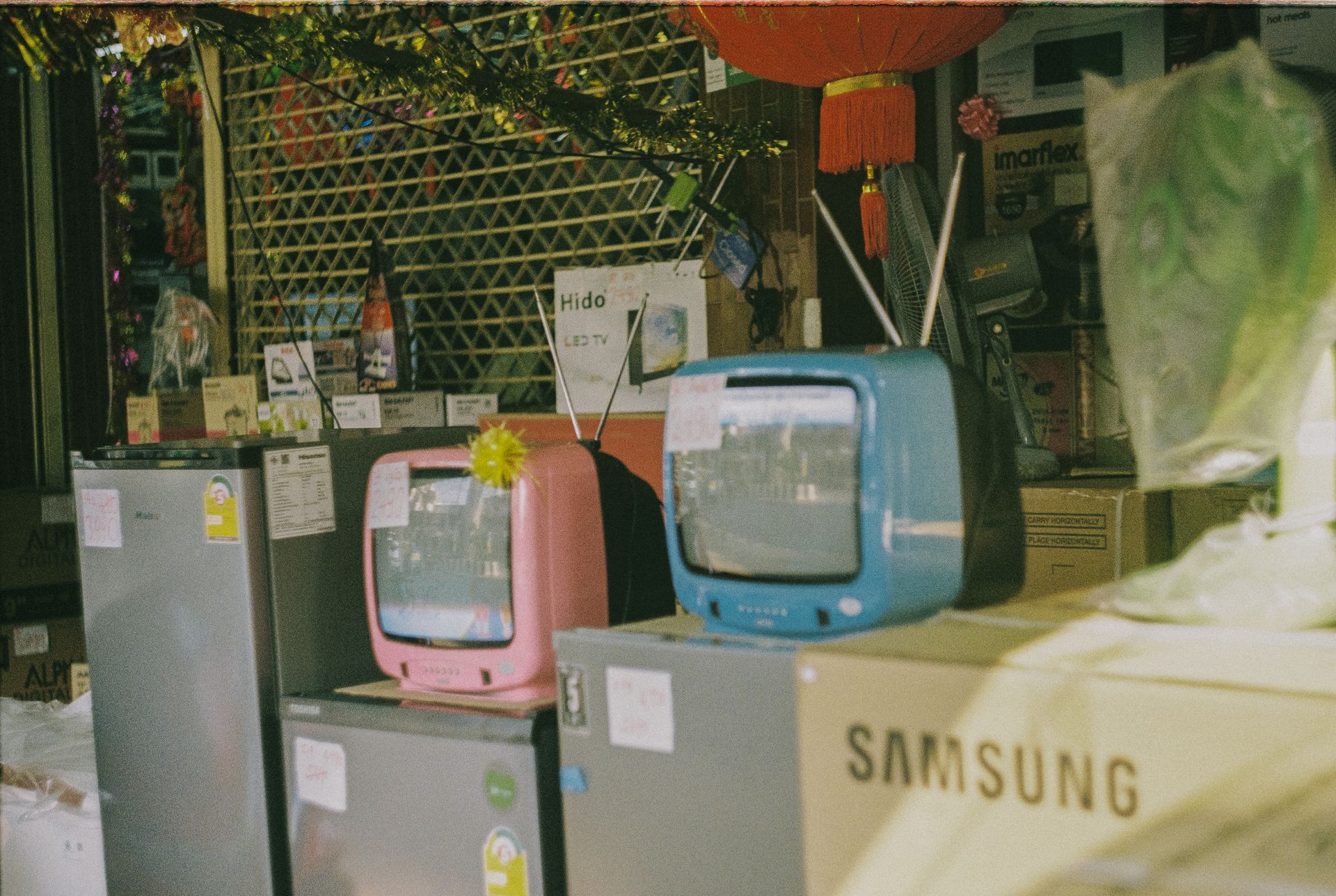 A storefront display featuring vintage televisions and home appliances on a sunny day in Bangkok.