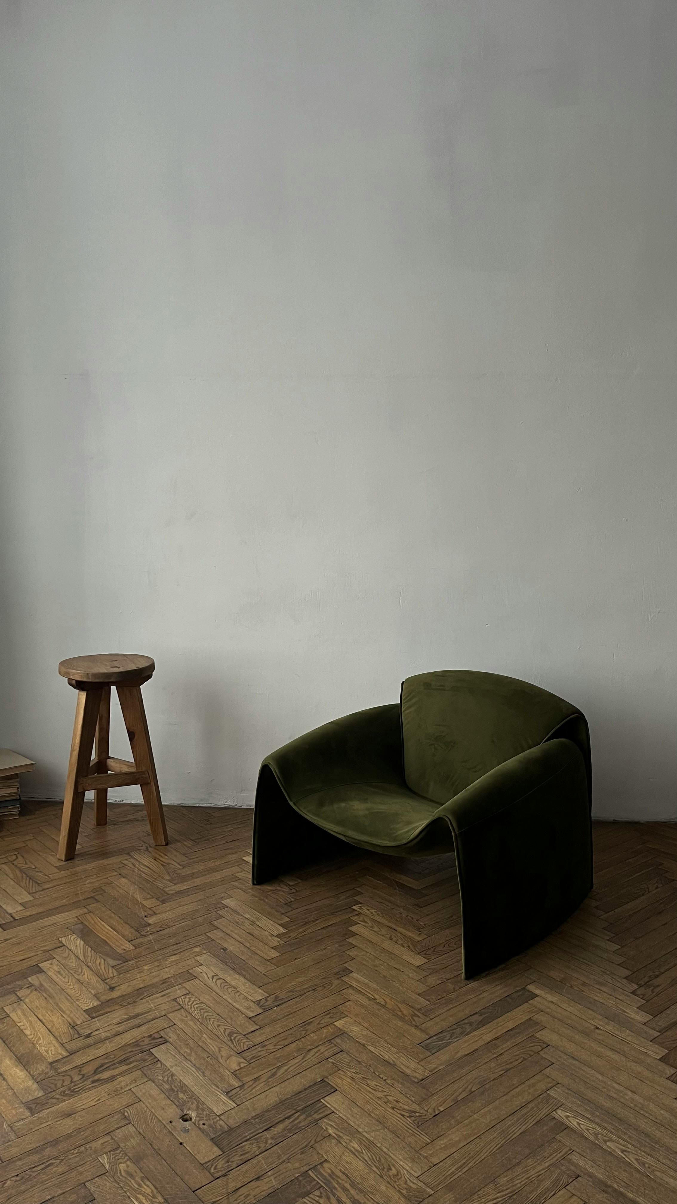 Free A minimalist interior featuring a modern green armchair and wooden stool on parquet flooring. Stock Photo
