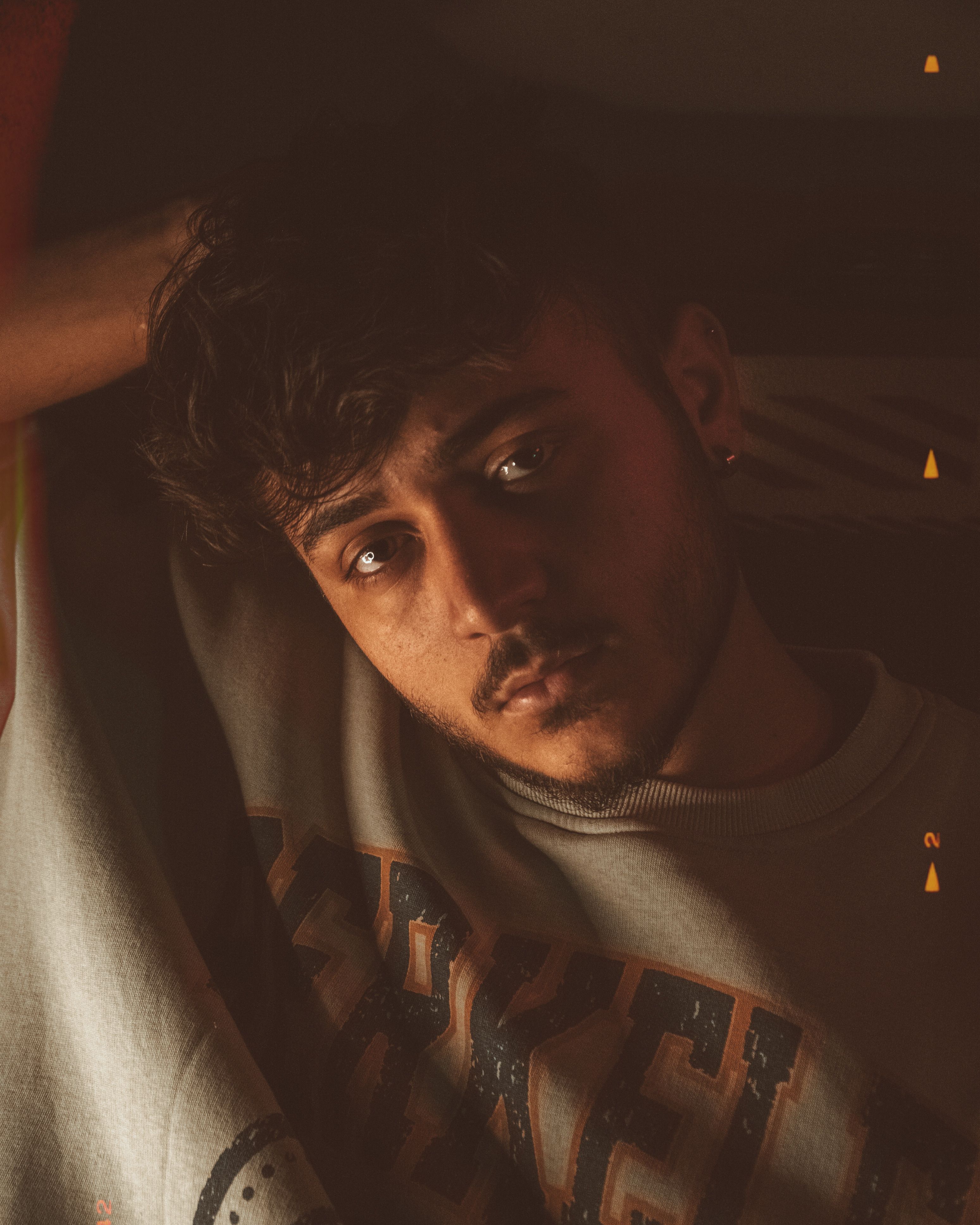 Close-up portrait of a young man with moody lighting indoors wearing a Berkeley sweatshirt.