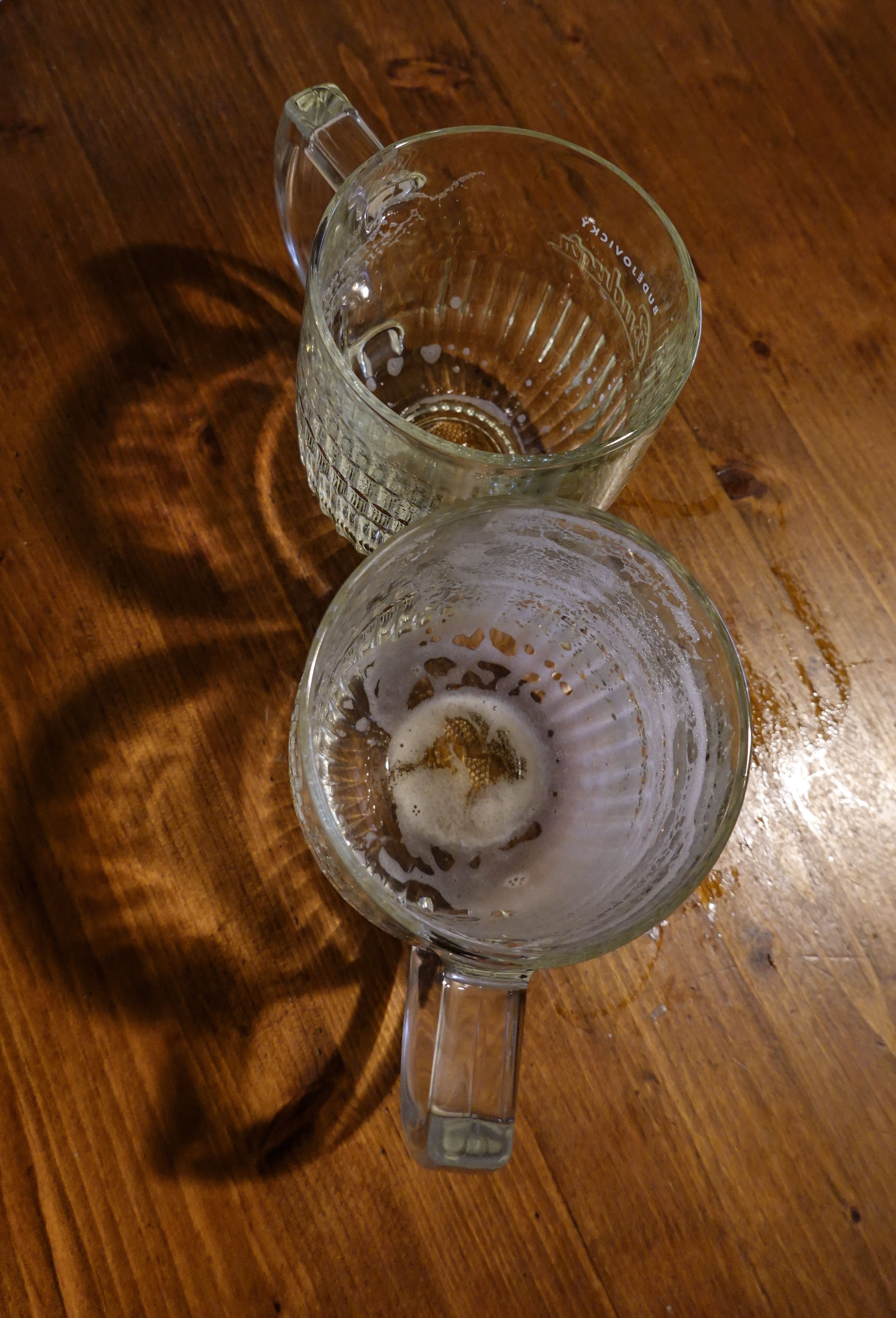 Top view of two empty beer mugs with foam remnants on a wooden table.