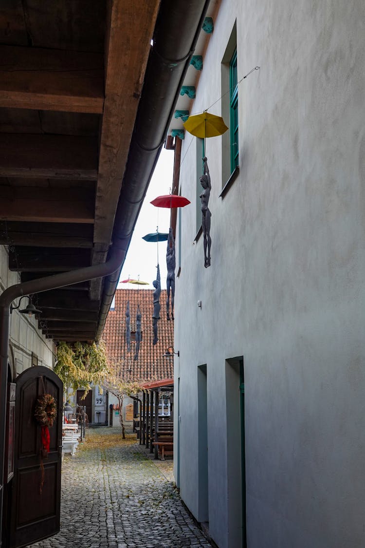 Figurines Hanging On Umbrellas Along A Narrow Passage