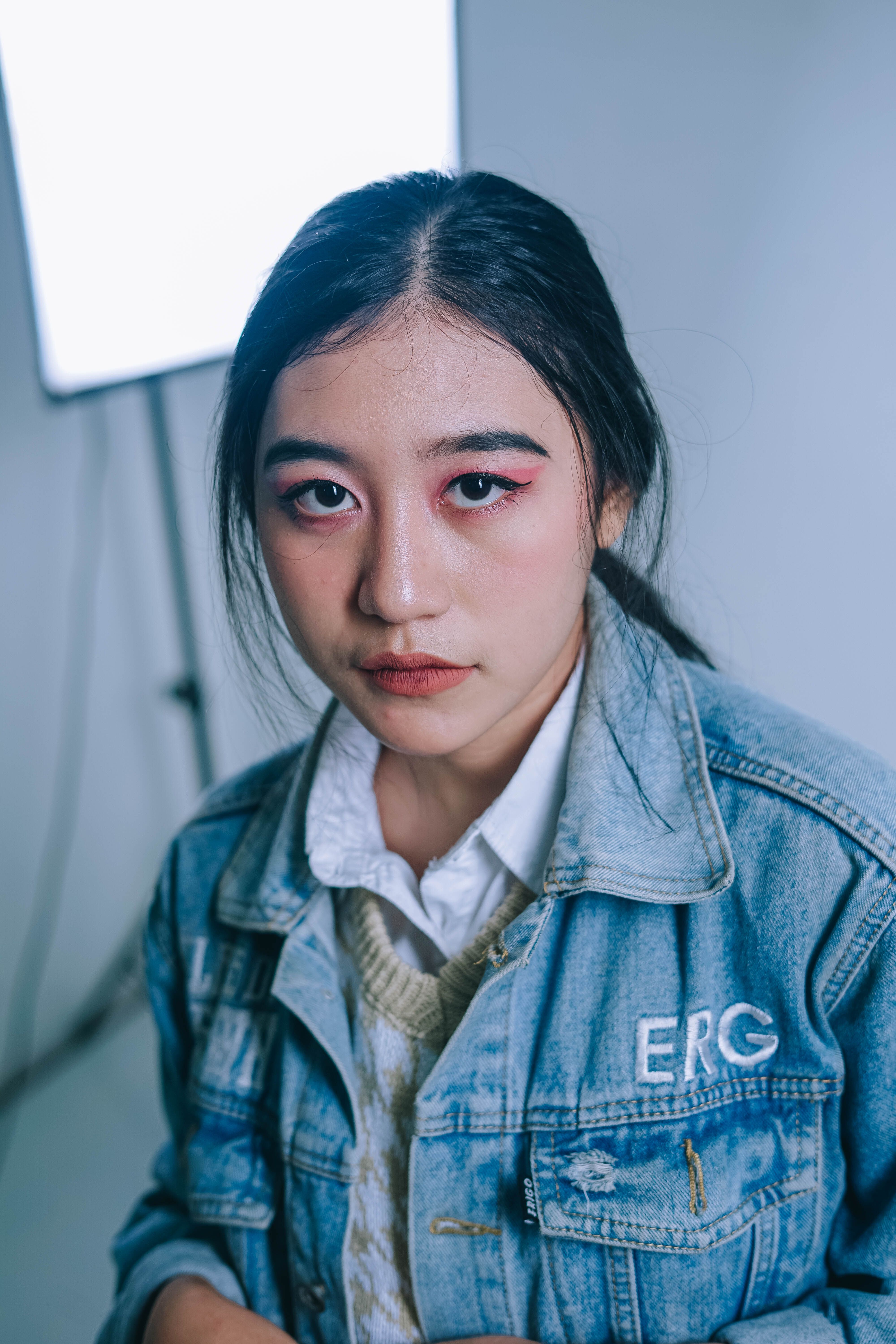 Fashion portrait of an adult woman wearing a denim jacket with bold makeup indoors.