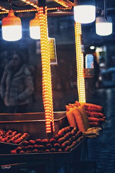Vibrant night scene of an illuminated corn cart offering fresh street food in an urban setting.
