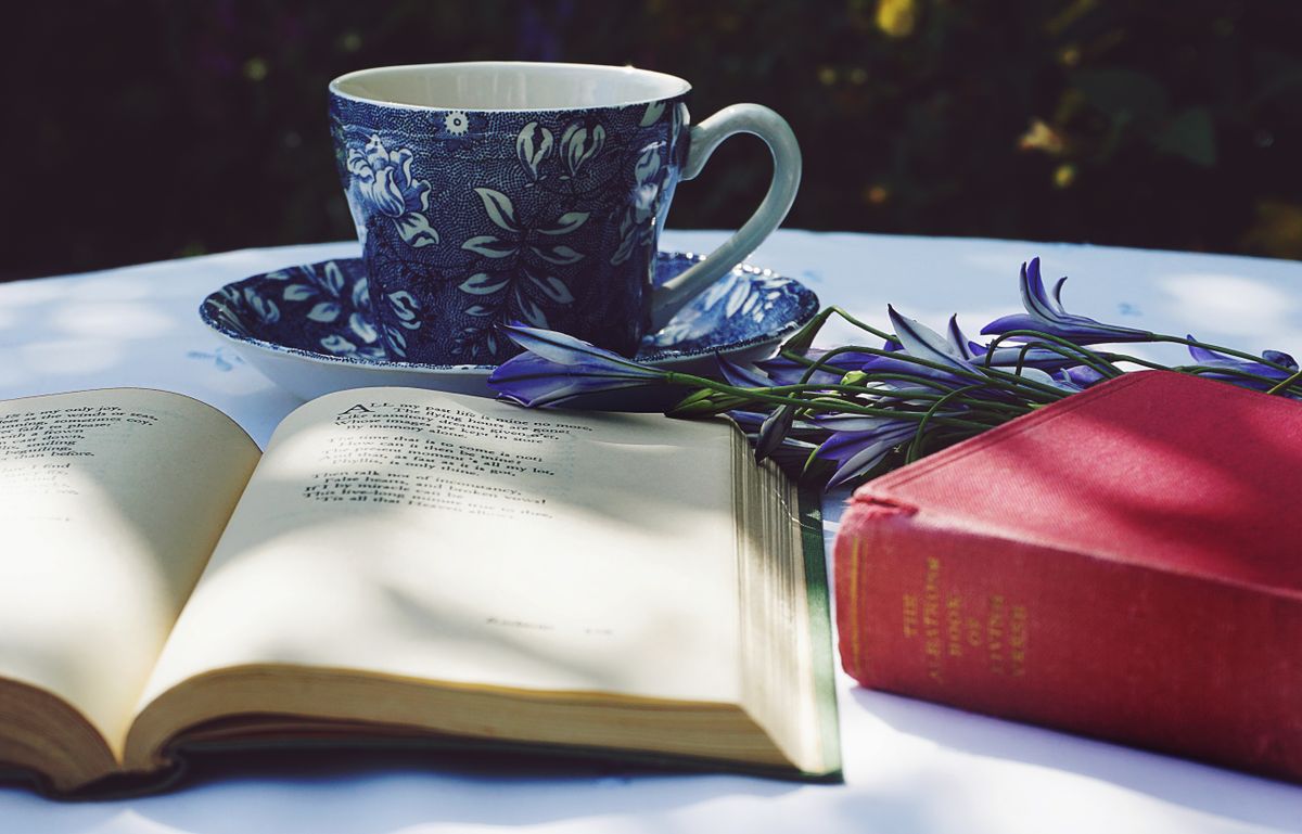 Small outdoor table with a book, tea cup, and flowers on top