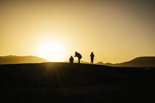 Three silhouetted figures on a desert dune at sunrise showcasing serene natural beauty.