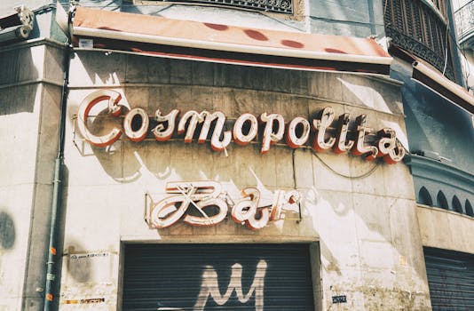Close-up view of 'Cosmopolita Bar' neon sign on an urban building facade with vintage style.