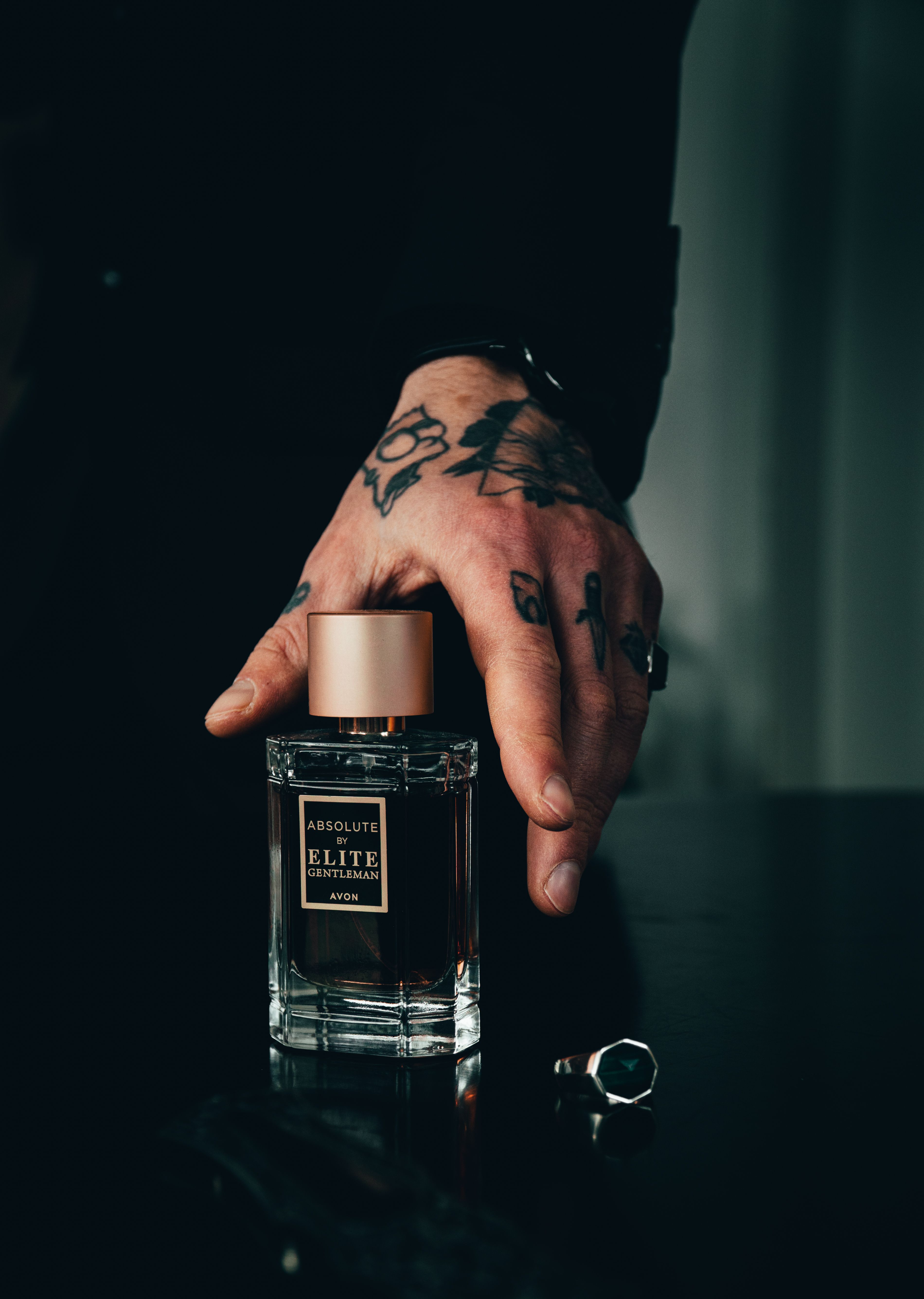 Man's hand holding a luxury cologne perfume bottle with dark moody background for men's fragrance editorial