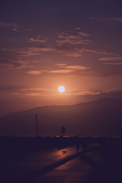 Free A beautiful sunset in Los Angeles with silhouettes of people walking along the road, creating a dramatic scene. Stock Photo