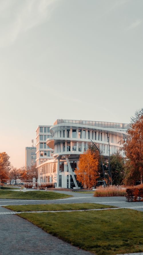 Free Vertical shot of a modern building surrounded by autumn foliage under a sunset sky. Stock Photo