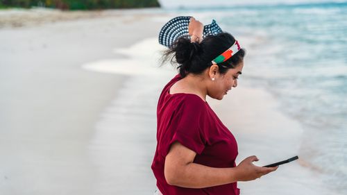Free A woman enjoying a beach day while checking her smartphone with a serene ocean view. Stock Photo