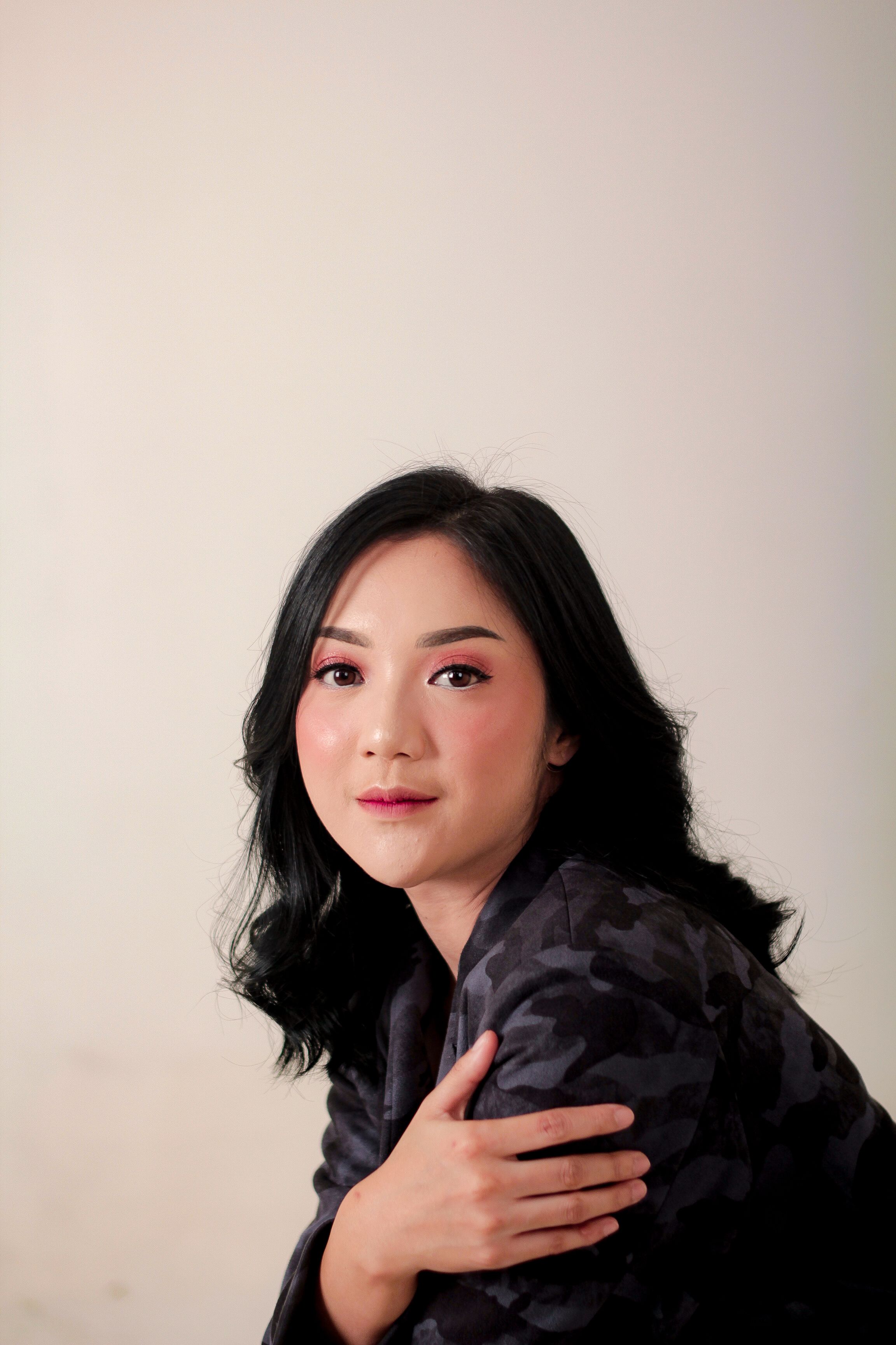 Chic studio portrait of a smiling Asian woman with dark hair in a stylish pose.