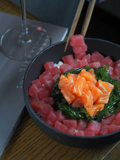A bowl of glossy, finely minced negitoro tuna mixed with chopped scallion, served over sushi rice with a swirl of soy sauce and a sprinkle of sesame seeds.