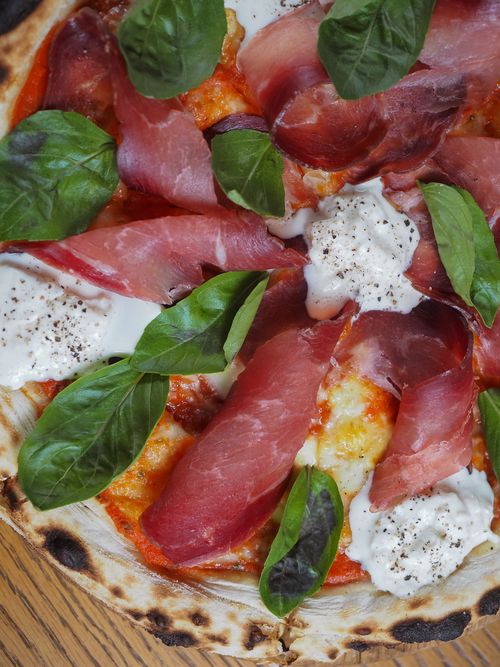 Free Close-up of a gourmet pizza topped with prosciutto, basil, and fresh mozzarella cheese. Stock Photo