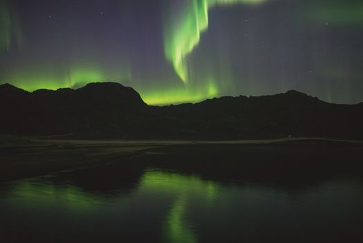 Northern lights illuminate the night sky over a tranquil lake and mountain landscape in Iceland.