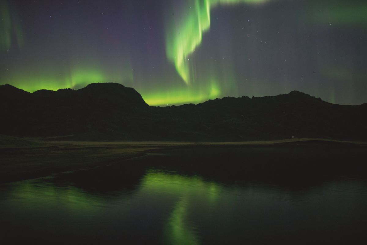 Green northern lights mirrored in a still lake