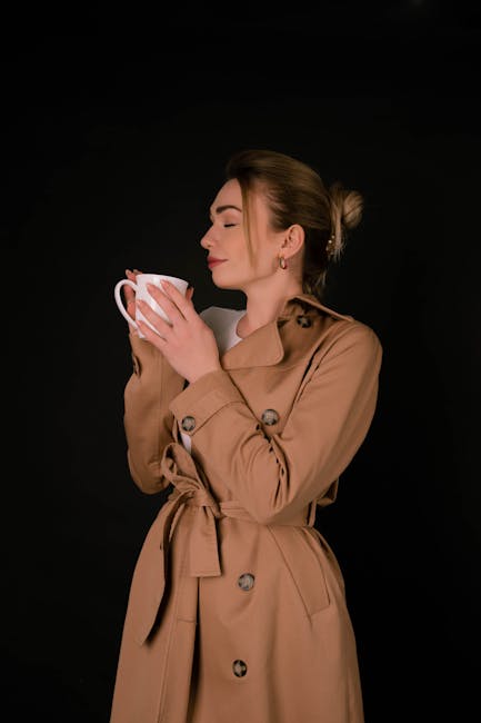 Fashionable woman in trench coat enjoying coffee in a studio setting.