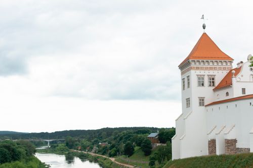 Free A regal castle with a red roof stands majestically by a river amidst lush greenery. Stock Photo