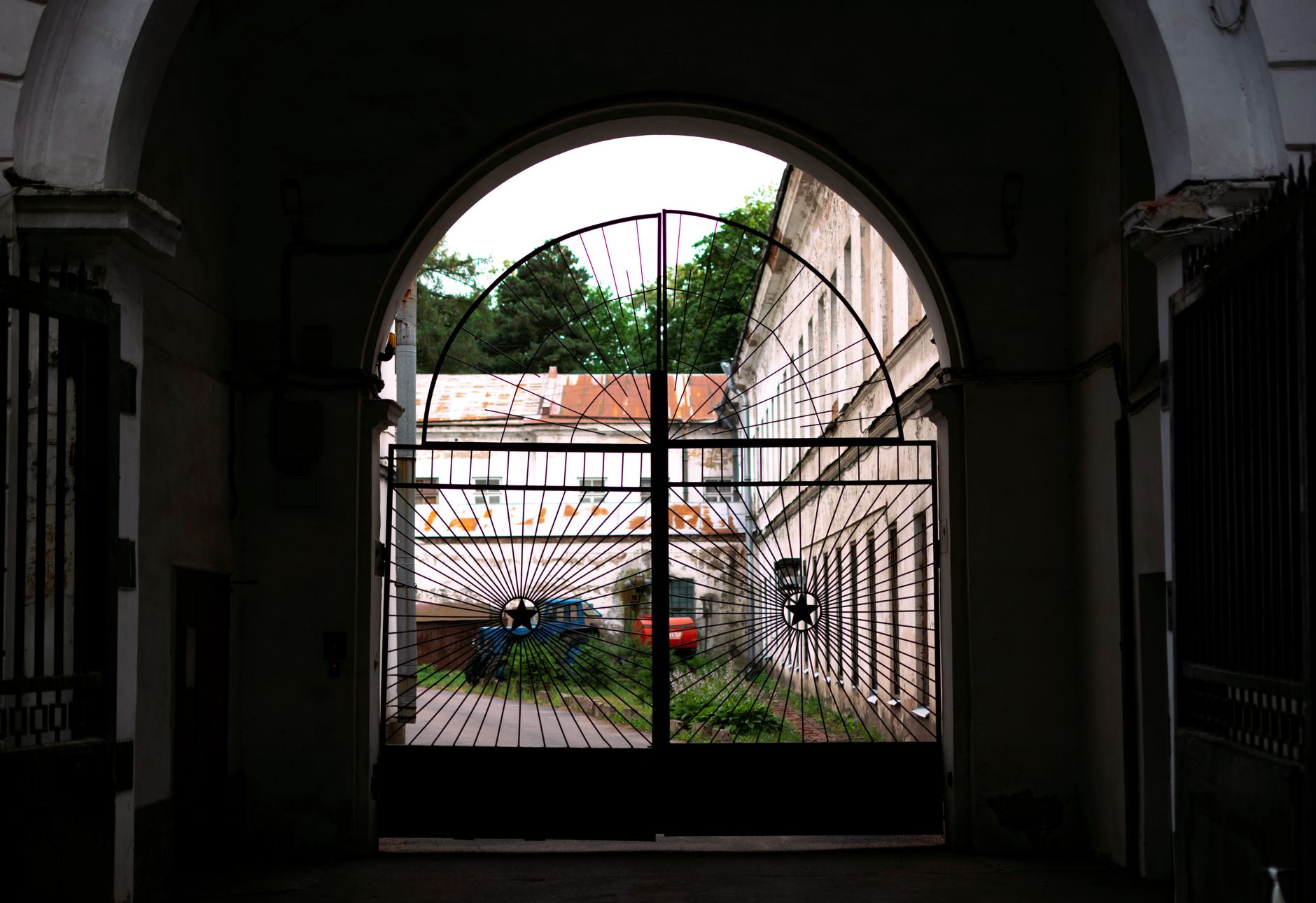 View through a decorative metal gate towards a historic courtyard with vehicles