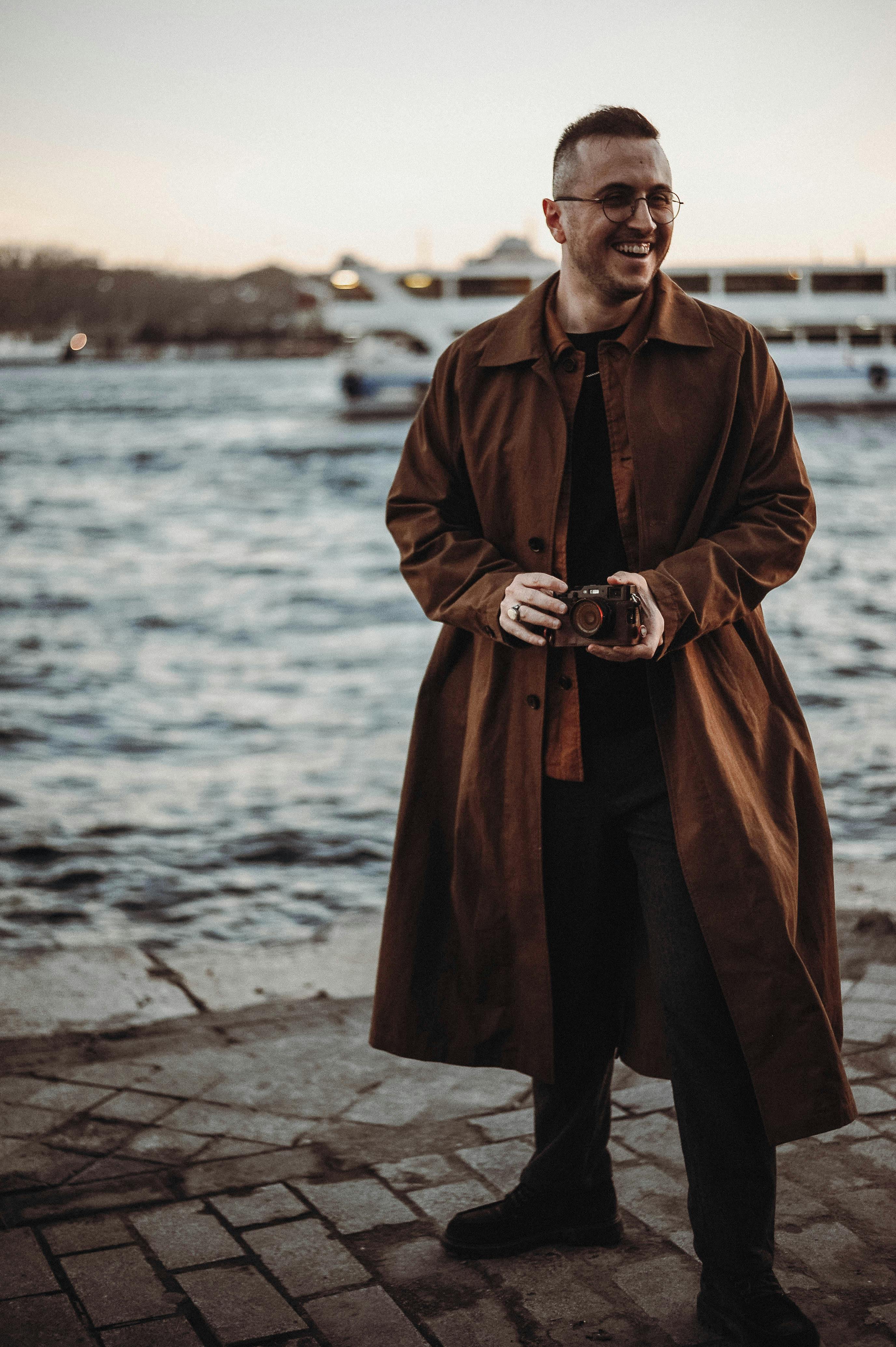 A stylish man holding a camera, enjoying the waterside view at sunset.