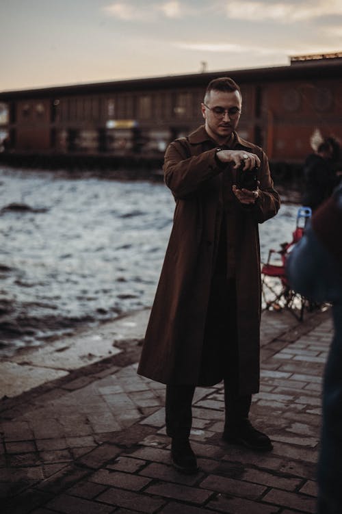 Man in Brown Coat Taking a Photo Using Black Camera