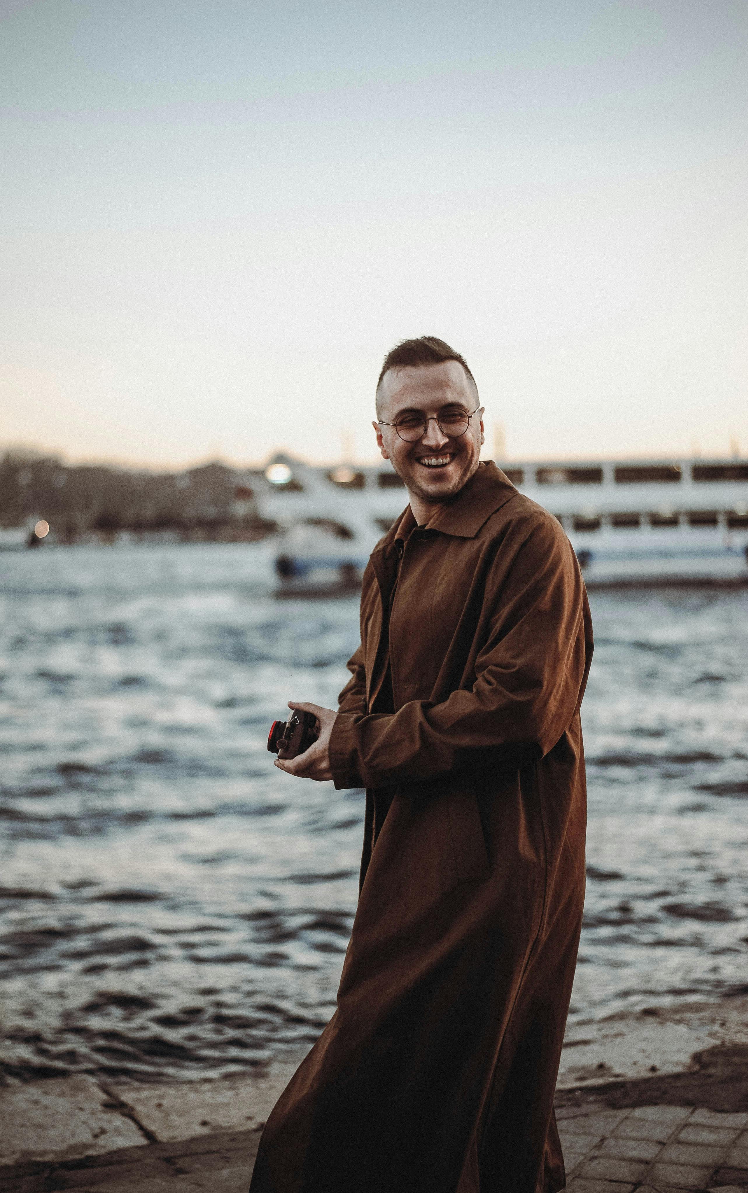 A cheerful man holding a camera by the riverside, enjoying a relaxing day outdoors.