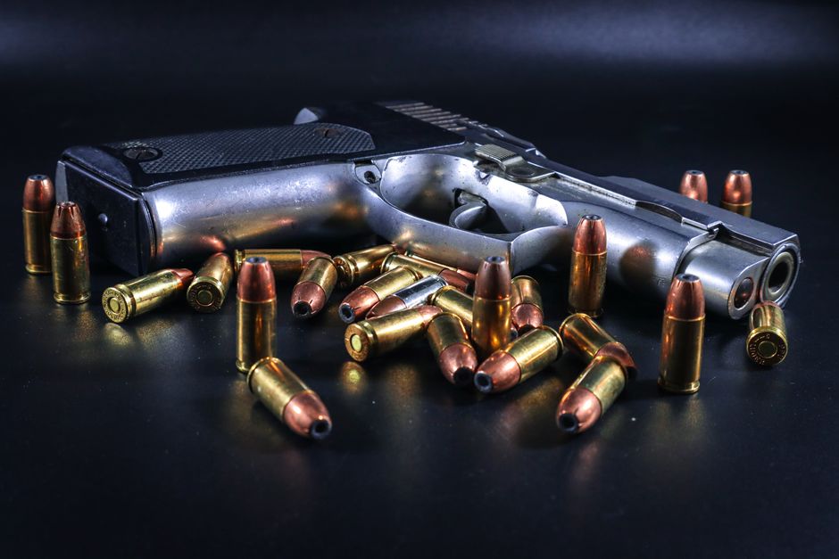 Fotomural Una pistola rodeada de balas de latón sobre un fondo negro, ideal para proyectos relacionados con armamento.