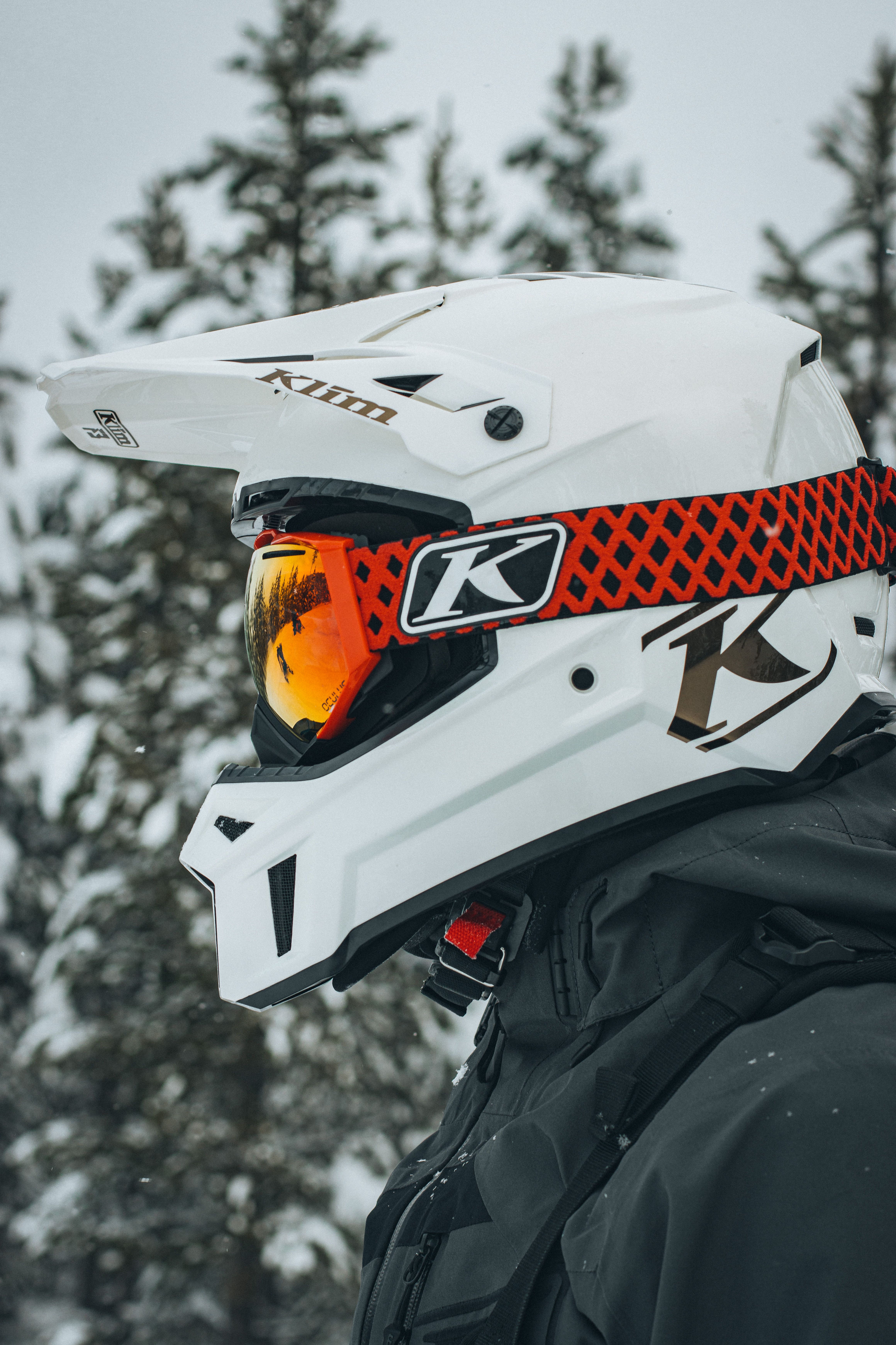 Detailed view of a protective snowmobile helmet with reflective visor amidst snowy trees.