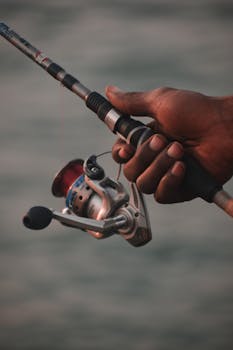 A detailed shot of a hand gripping a fishing rod by a calm shoreline in Lagos, Nigeria.