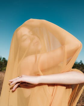 Artistic portrait of a woman wrapped in orange tulle against a clear blue sky, capturing a serene and ethereal mood.