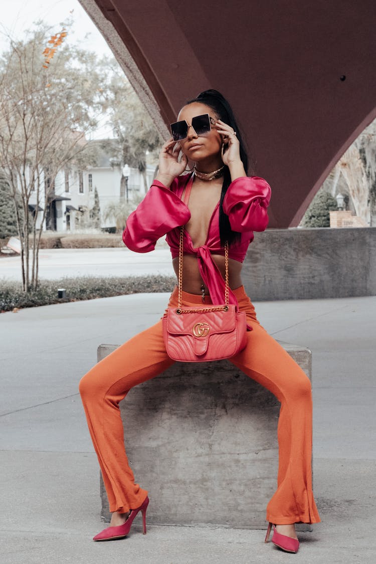 Woman In A Pink Tank Top And Orange Pants Sitting Under A Bridge