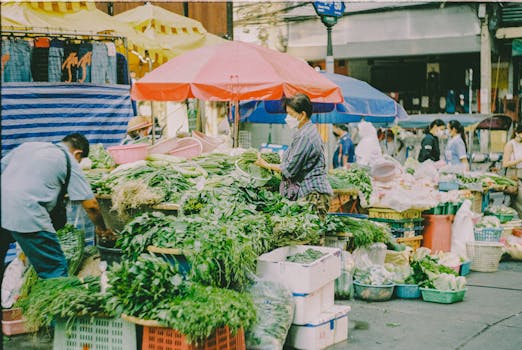 Bustling street market scene featuring vendors with fresh vegetables and colorful umbrellas.