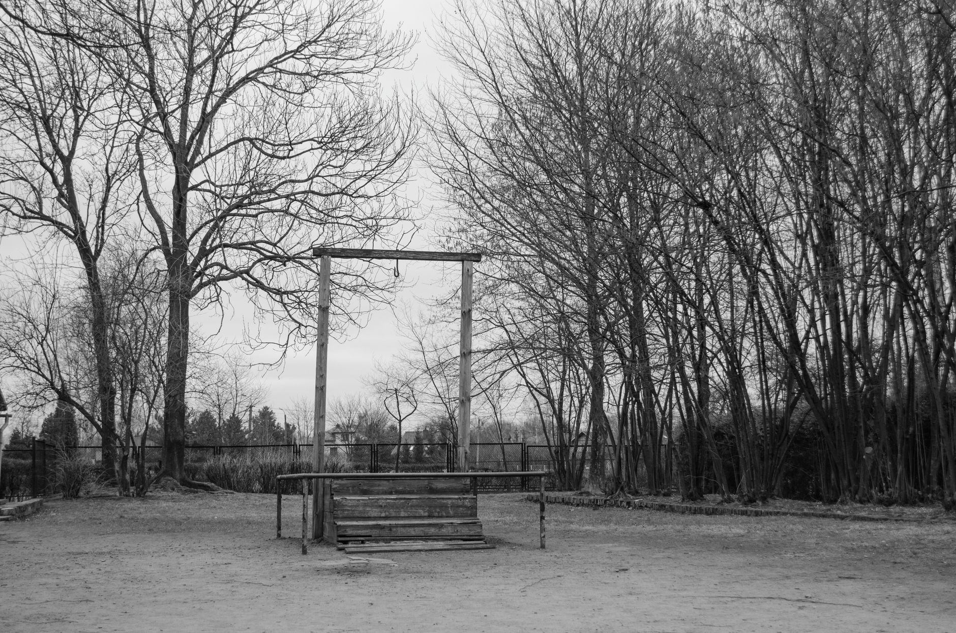 Black and white photo of a historic wooden gallows surrounded by bare trees.