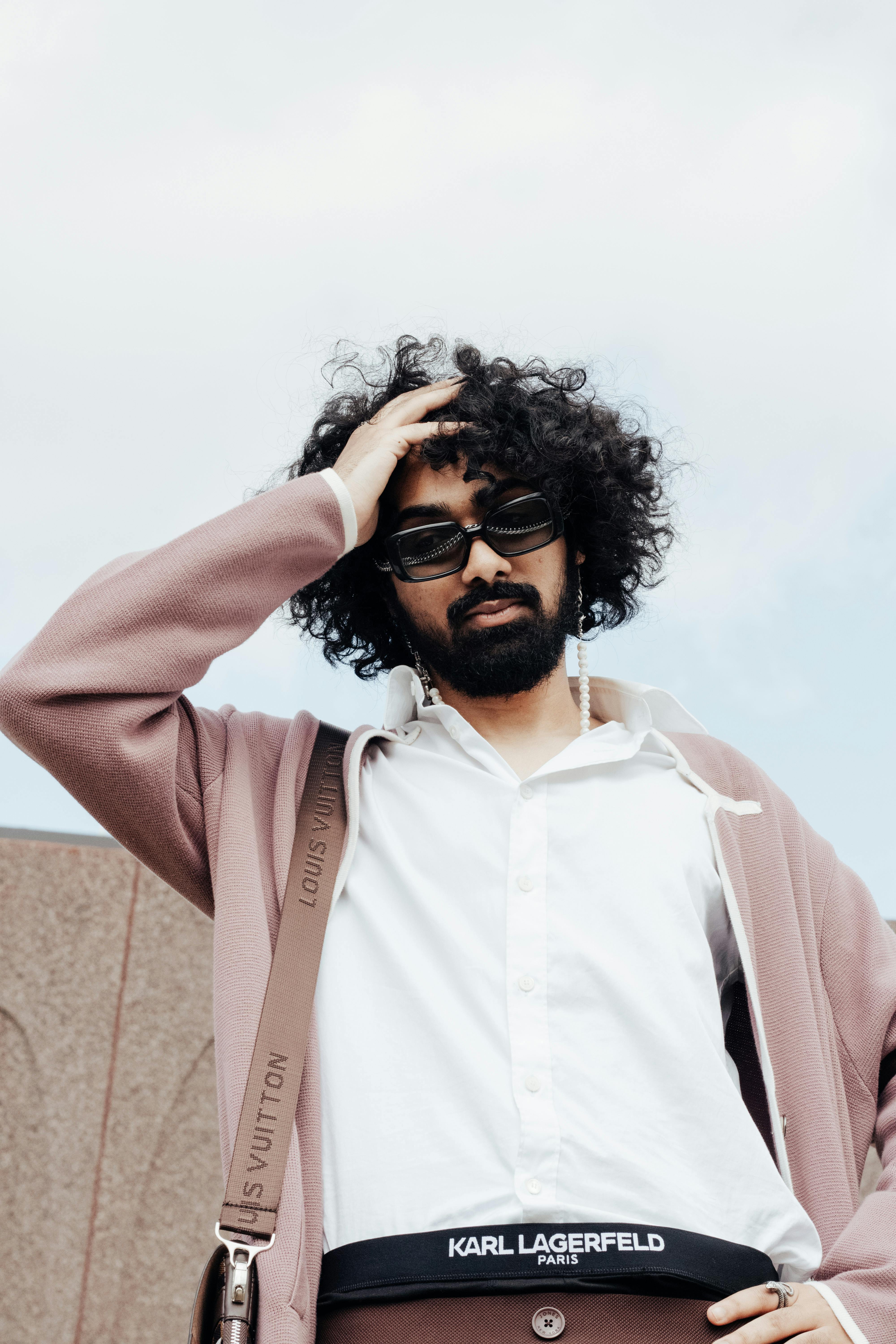 Portrait of a fashionable man with curly hair and sunglasses, exuding modern style.