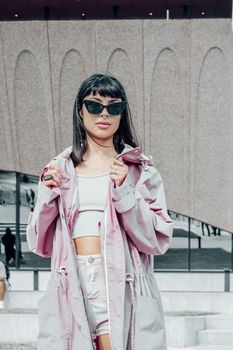 Stylish woman in sunglasses and pink outfit posing outdoors.