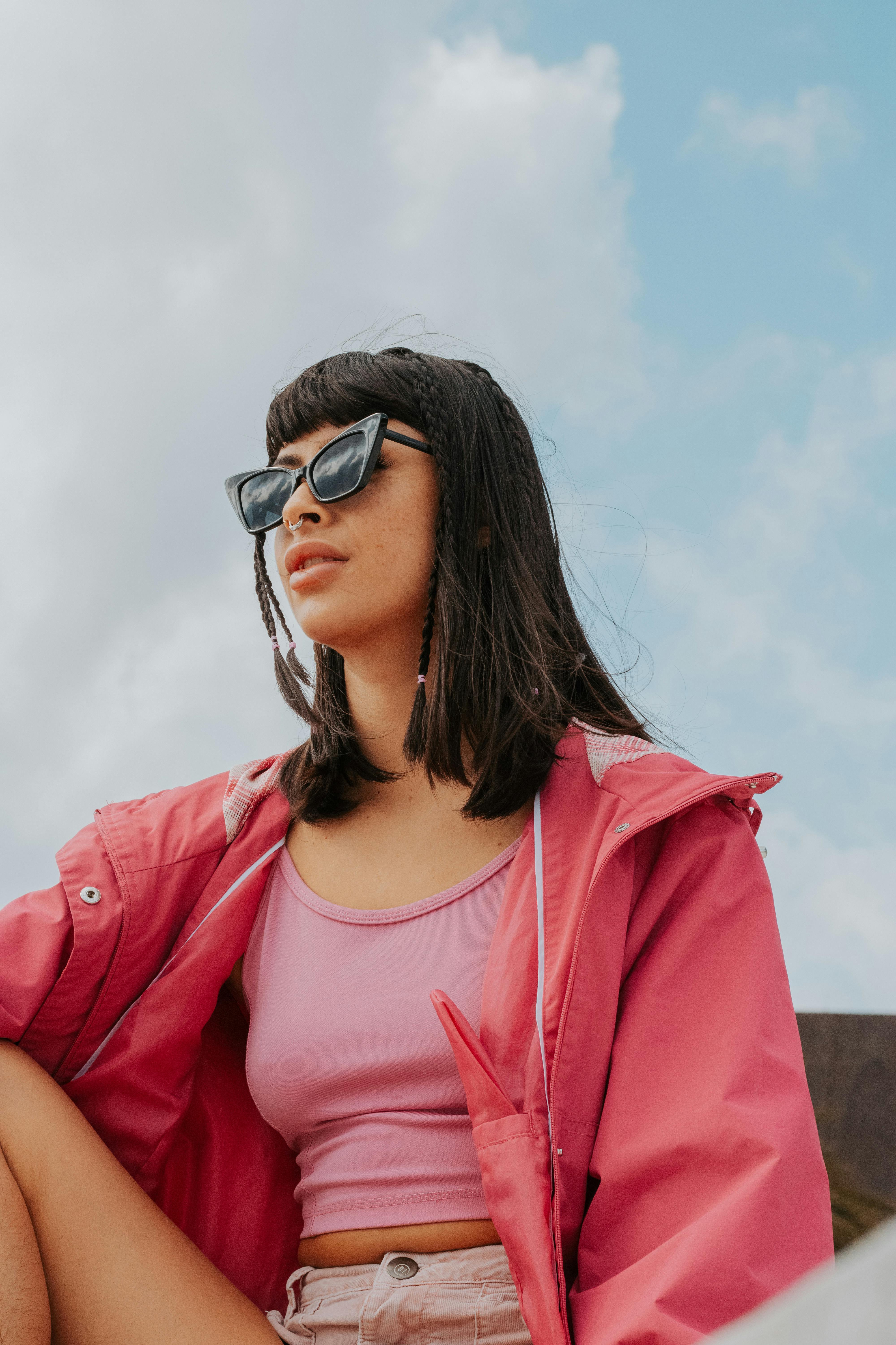 Woman wearing pink clothing and sunglasses, relaxing outdoors under a blue sky.