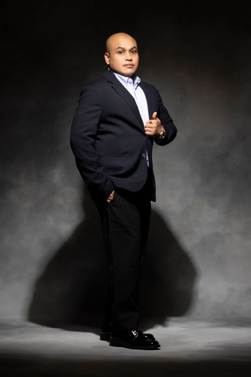Free Portrait of a bald South Asian man in a black suit, standing confidently in a studio setting. Stock Photo