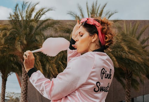 A Woman in Pink Jacket Holding a Cotton Candy with Her Tongue Out