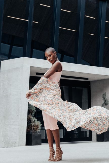 Stylish woman posing in a flowing dress outside a modern downtown building.