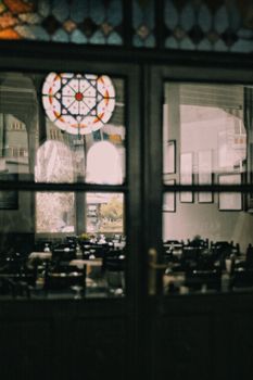 View of a beautifully decorated restaurant interior through glass doors, featuring stained glass elements.