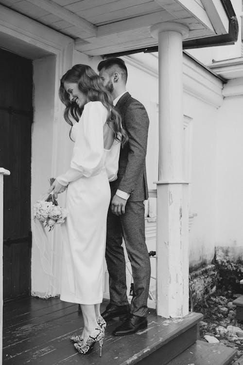Grayscale Photography of a Newlywed Couple Standing Near Wooden Door