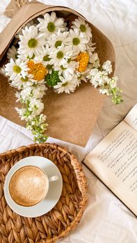 A relaxing scene of coffee, a floral bouquet, and an open book on a woven tray.